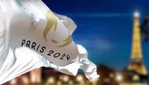 Paris 2024 Olympic flag waving with blurred Paris skyline at night.